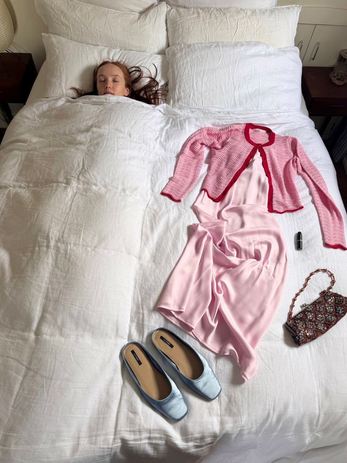 A pink cardigan set, flats and a small bag laid out on a white bed