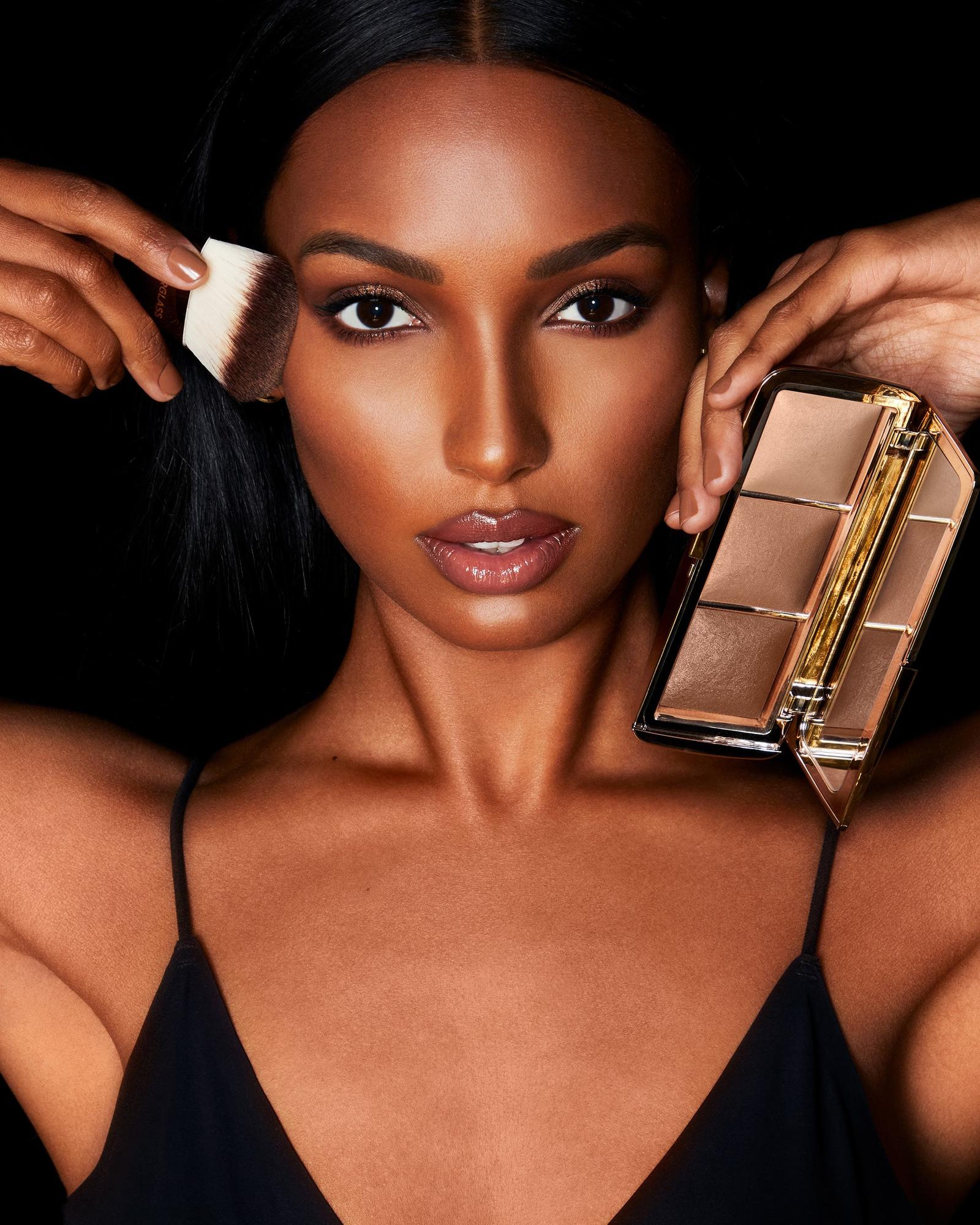 Woman in a black slip dress holding an Hourglass palette and a brush up to her face
