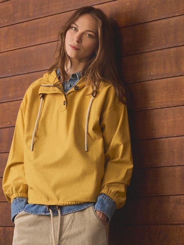 Woman in a yellow pullover layered over chambray against wood siding