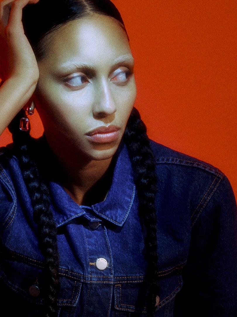 Model in a denim jacket against a deep red studio backdrop