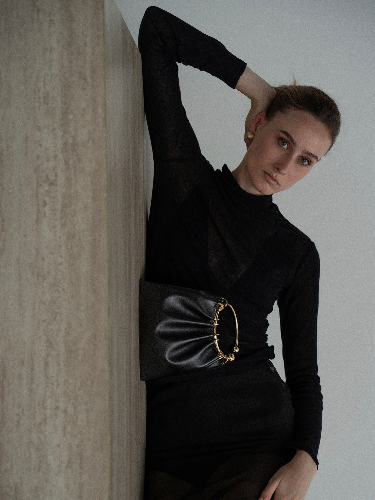 Model in a black dress wearing a sculptural VERAFIED clutch against a stone wall