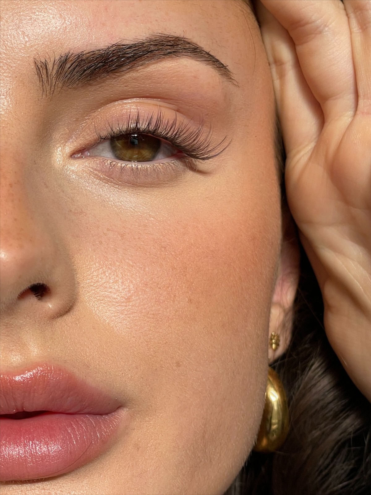 Woman holding a black lash serum tube up to her chin, eyes done in mascara