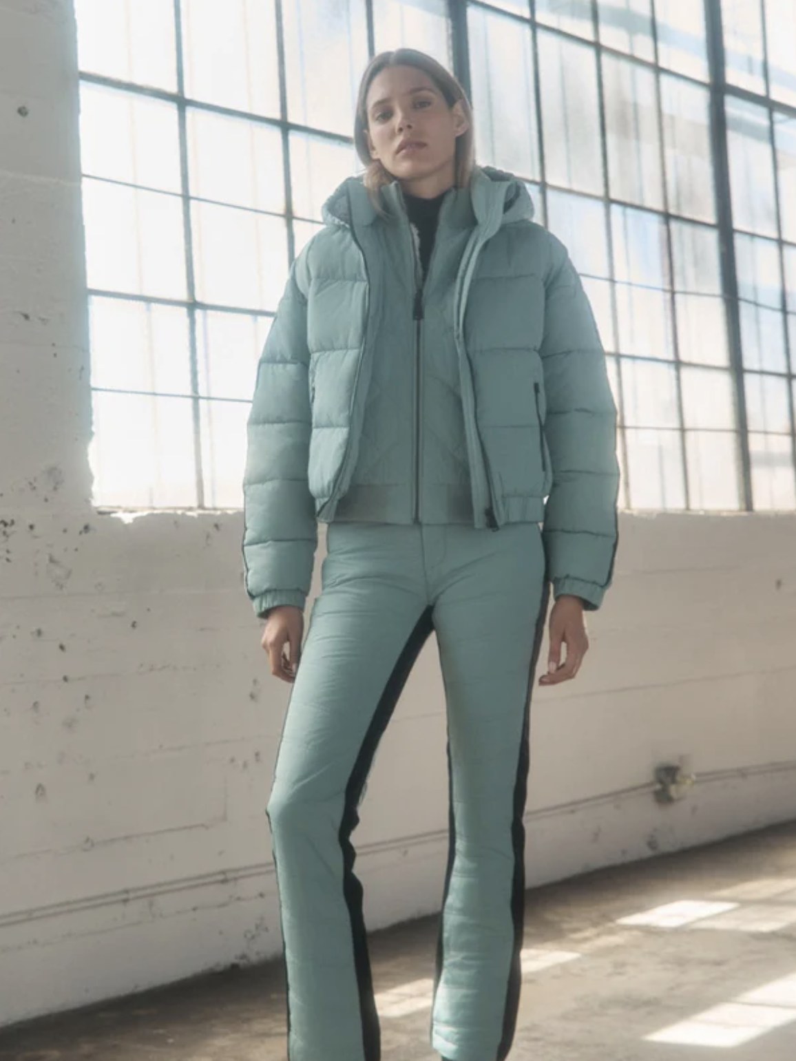 Model in a pale blue puffer jacket and matching pants in a sunlit studio