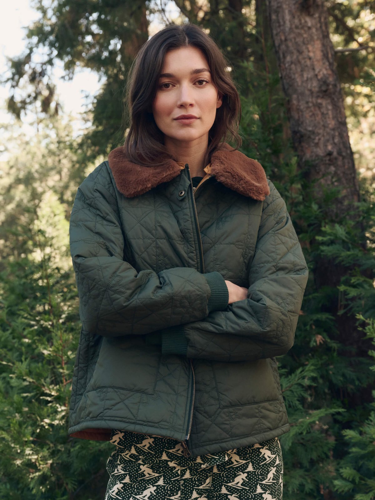 Model in a quilted green jacket and patterned bottoms among trees