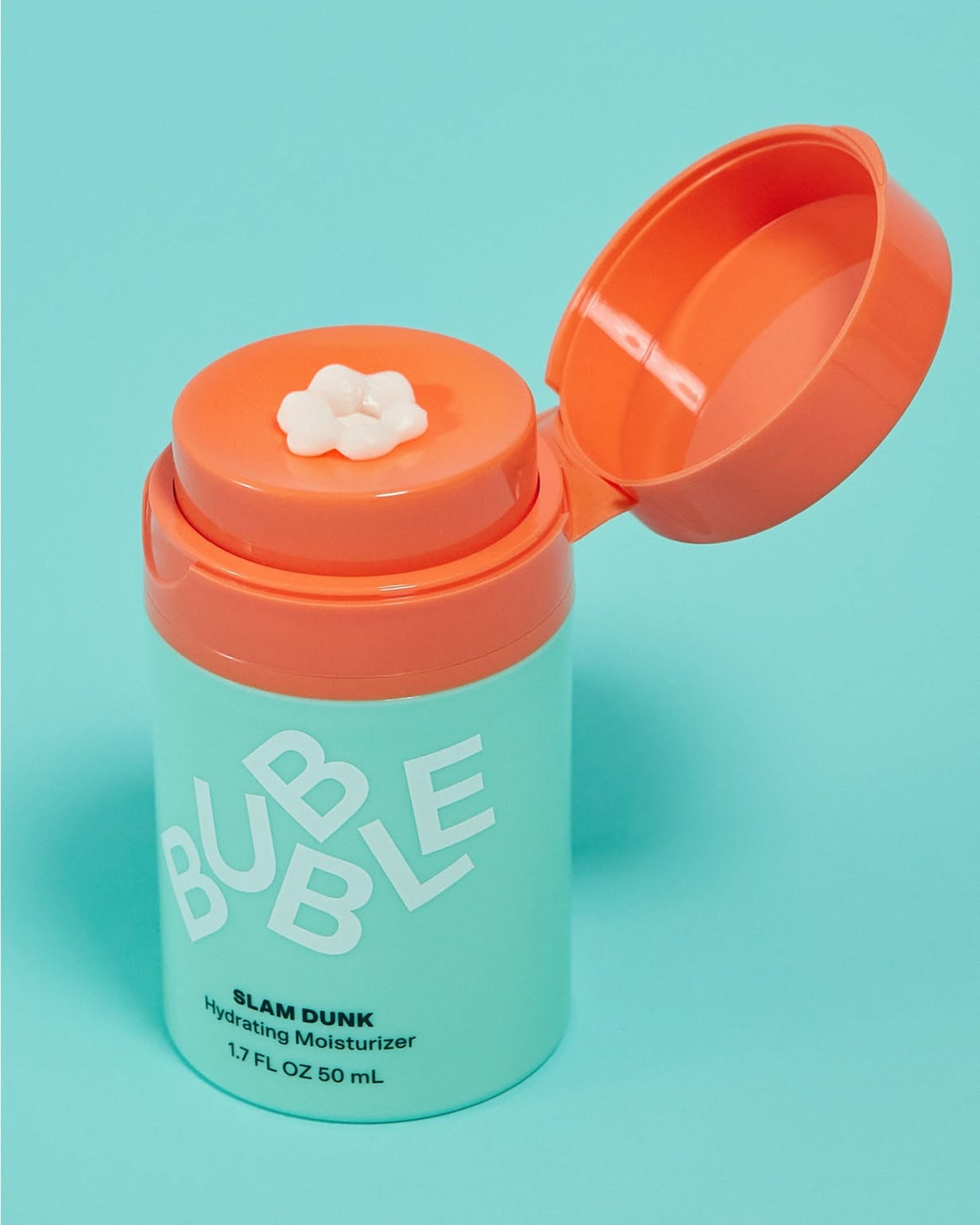 Bubble Slam Dunk Hydrating Moisturizer in a mint green bottle with an orange lid open, a small swirl of white cream on the pump, against a turquoise background.