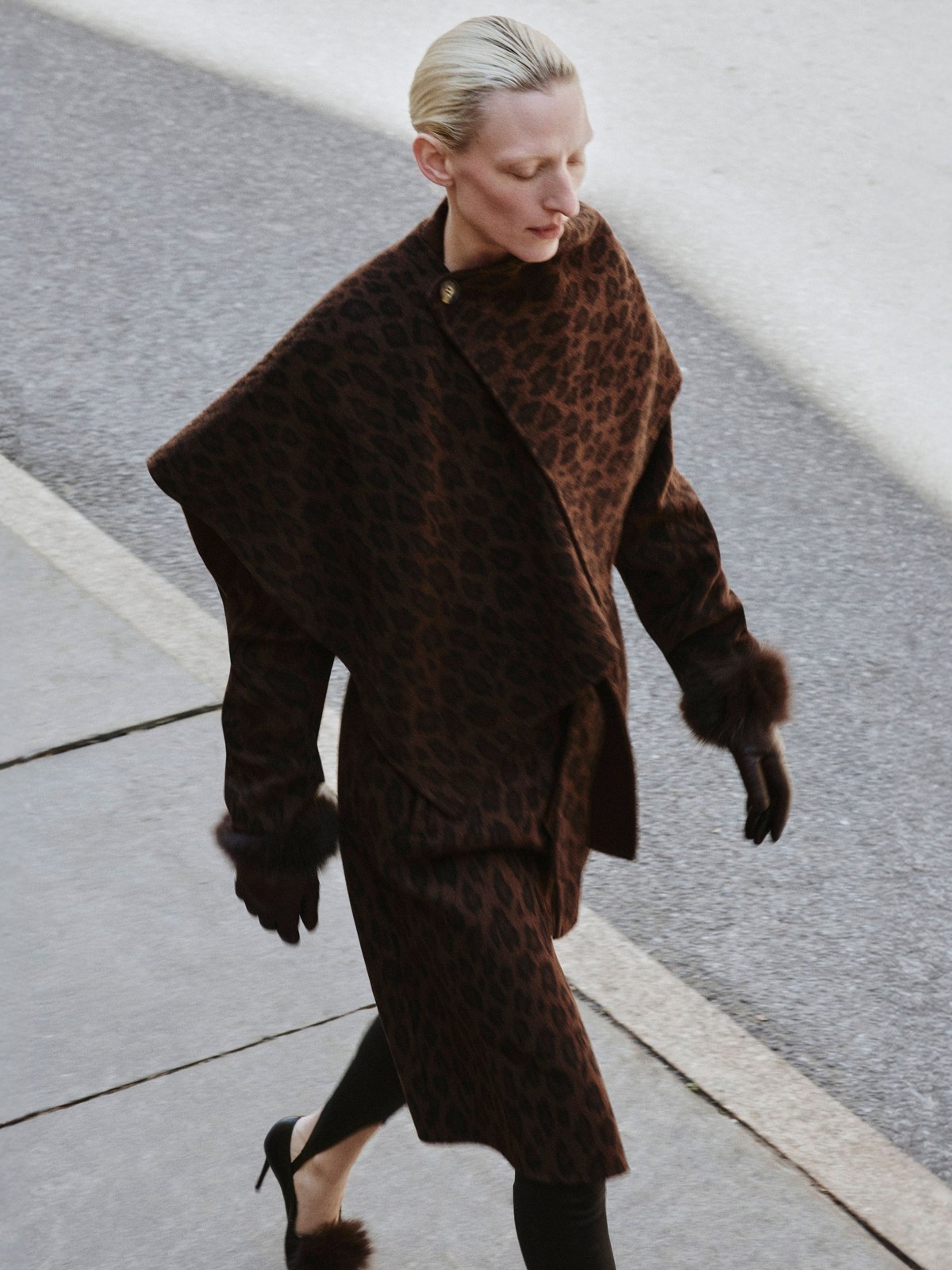 Model walking in a dark brown leopard outer layer on city pavement