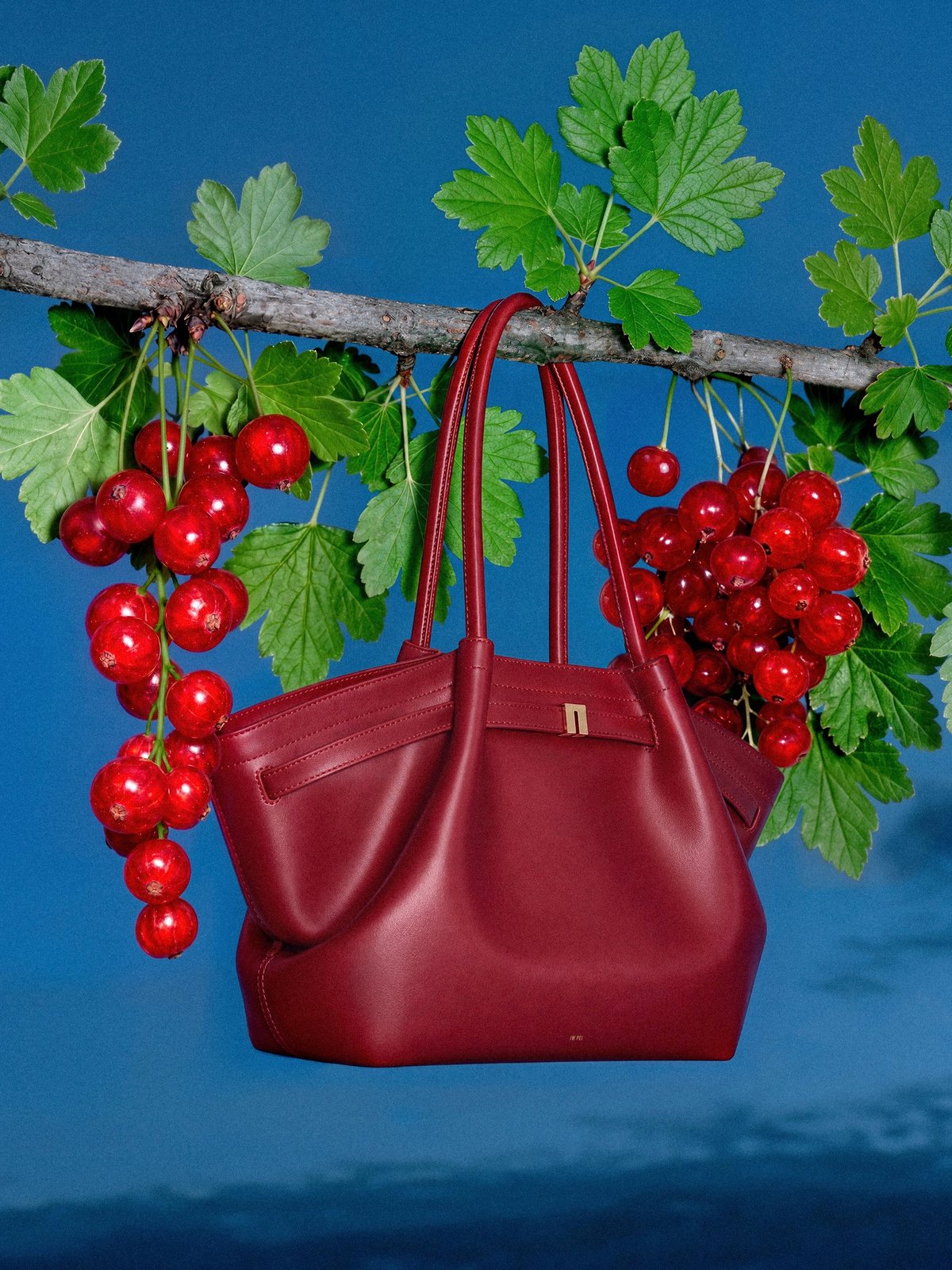 Red JW PEI tote among red currants under a blue sky