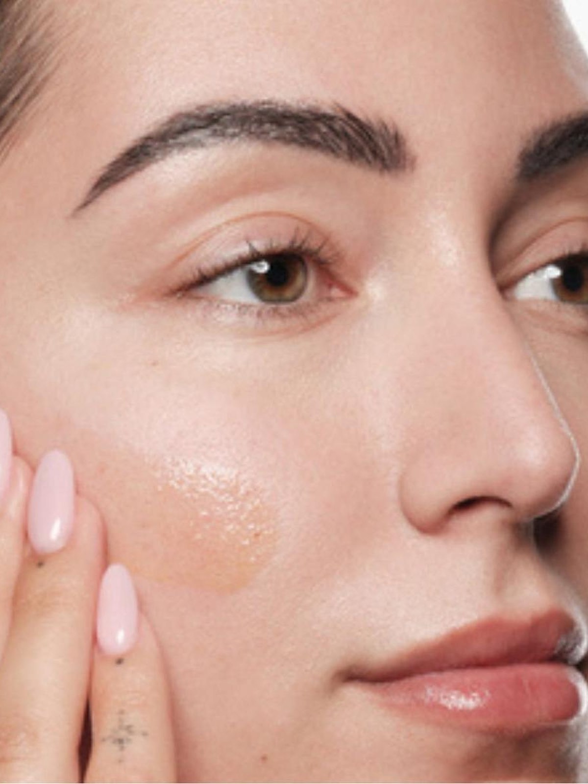 Close up of a woman with glowing skin and a hand on her cheek