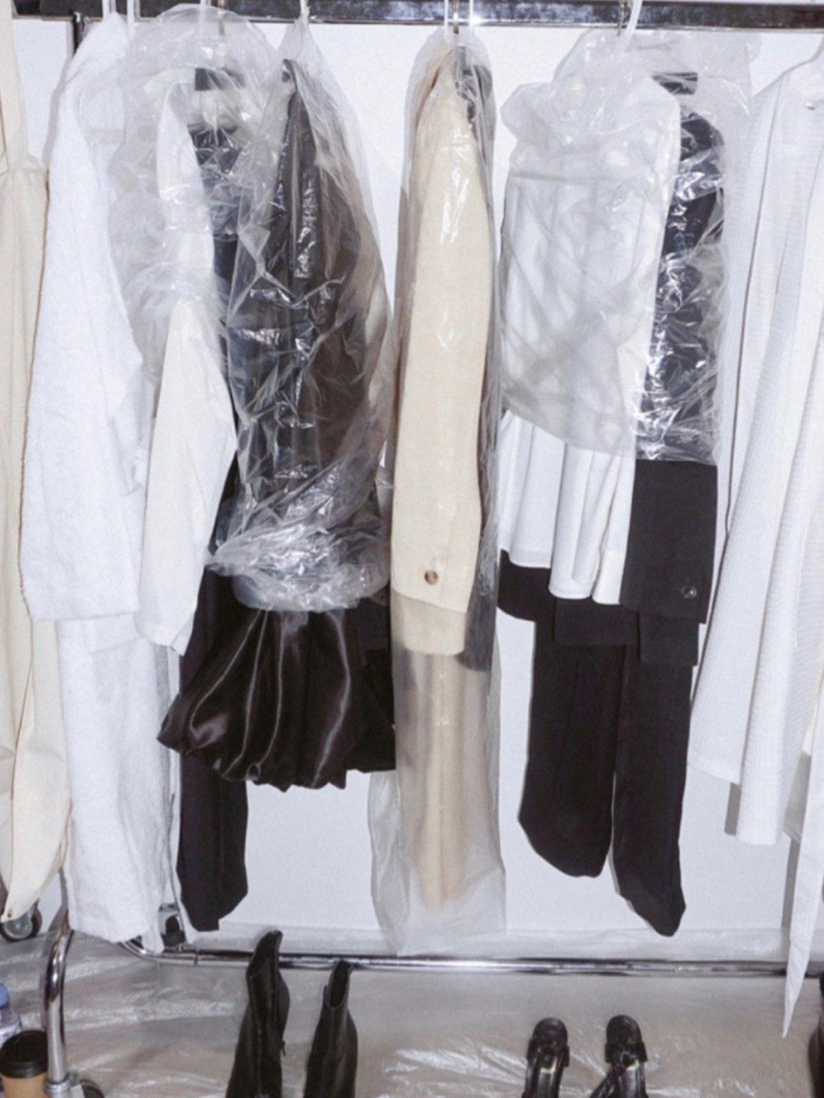 Garment bags and black heels lined up under a rail