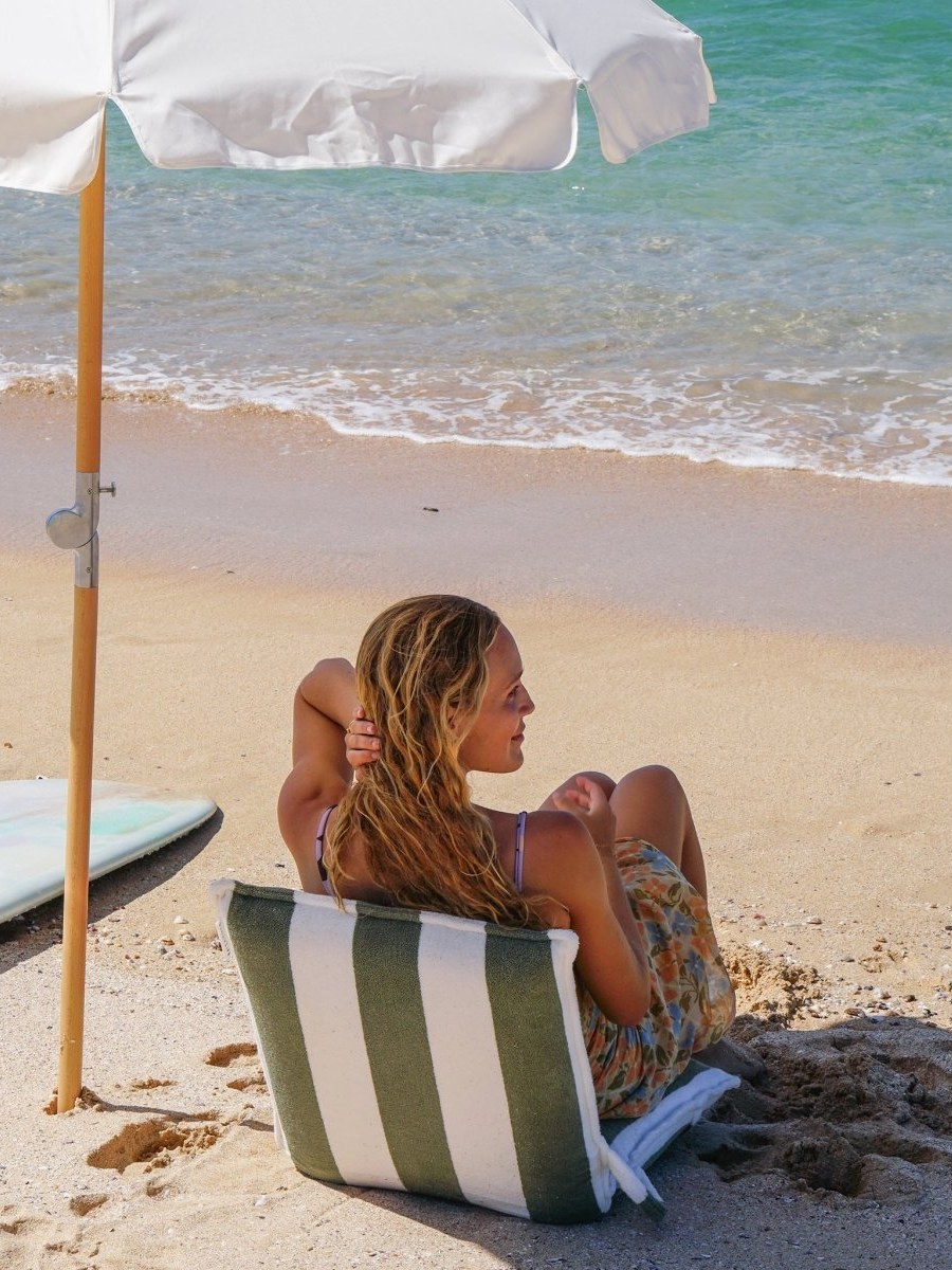 Woman reclining in a striped beach chair beneath an umbrella