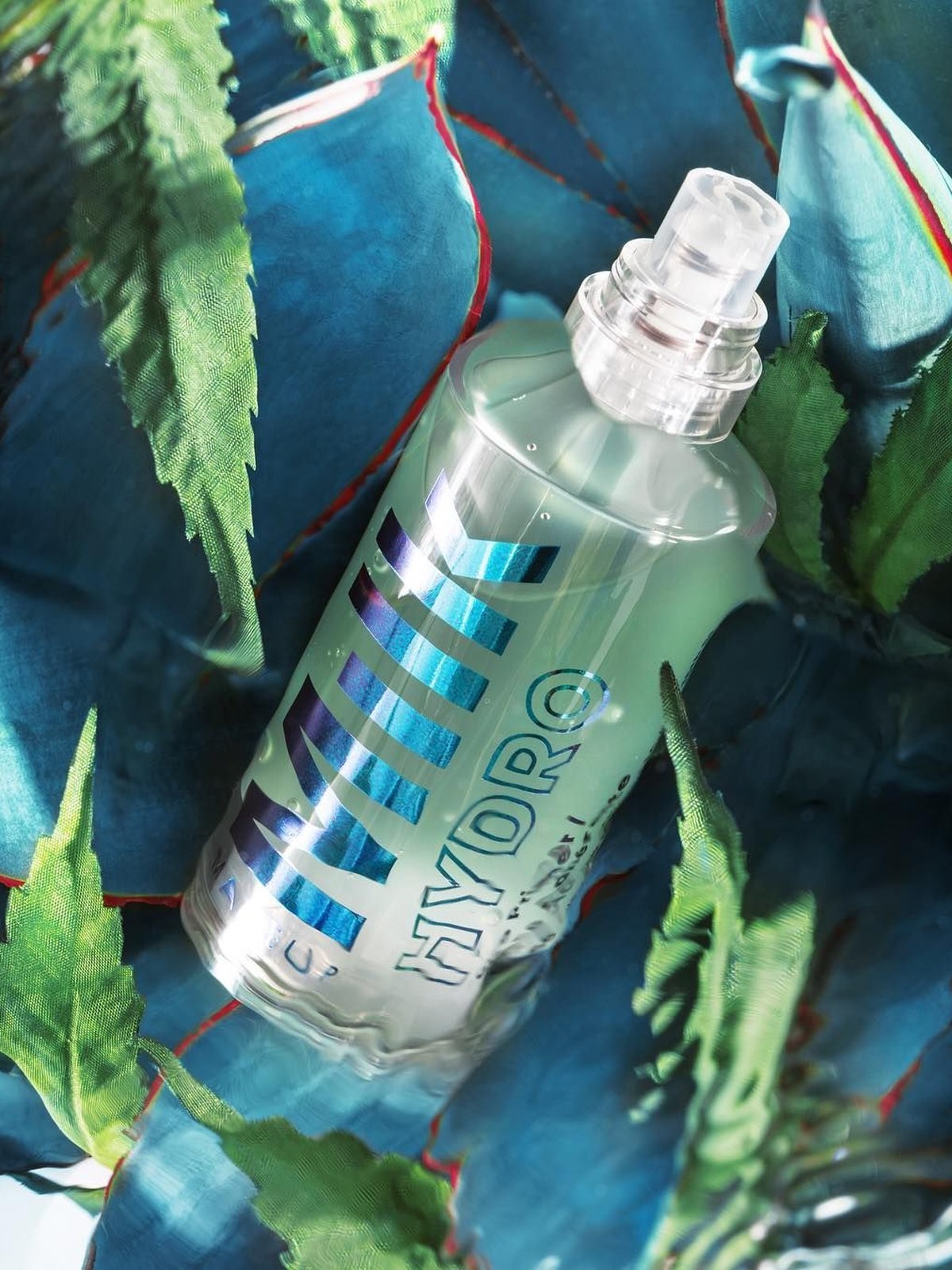 Milk Makeup Hydro spray bottle lying among blue-green agave leaves in sunlight