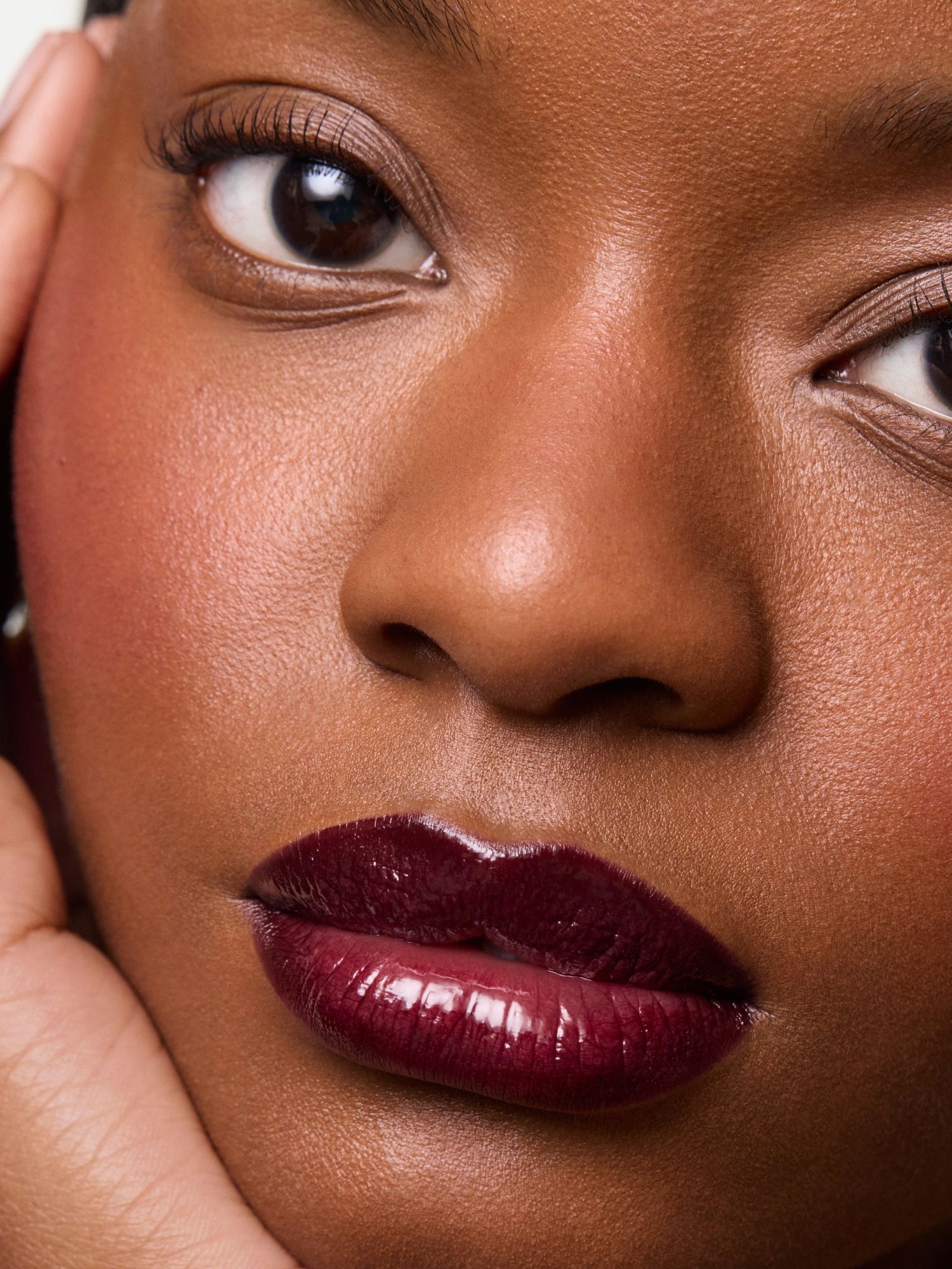 Woman with deep berry glossy lips and a hand on her cheek