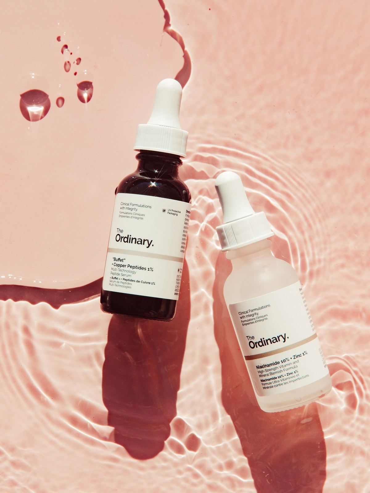 The Ordinary Buffet and Niacinamide bottles lying in pink-tinted rippling water