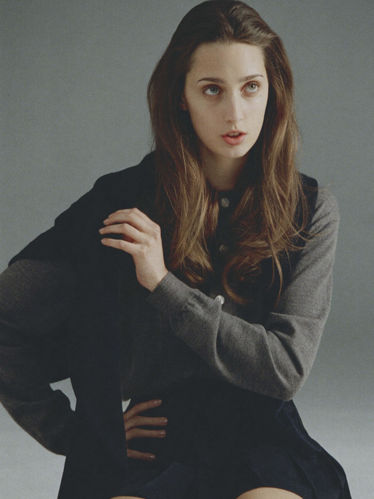Model seated in a dark outfit against a grey studio backdrop