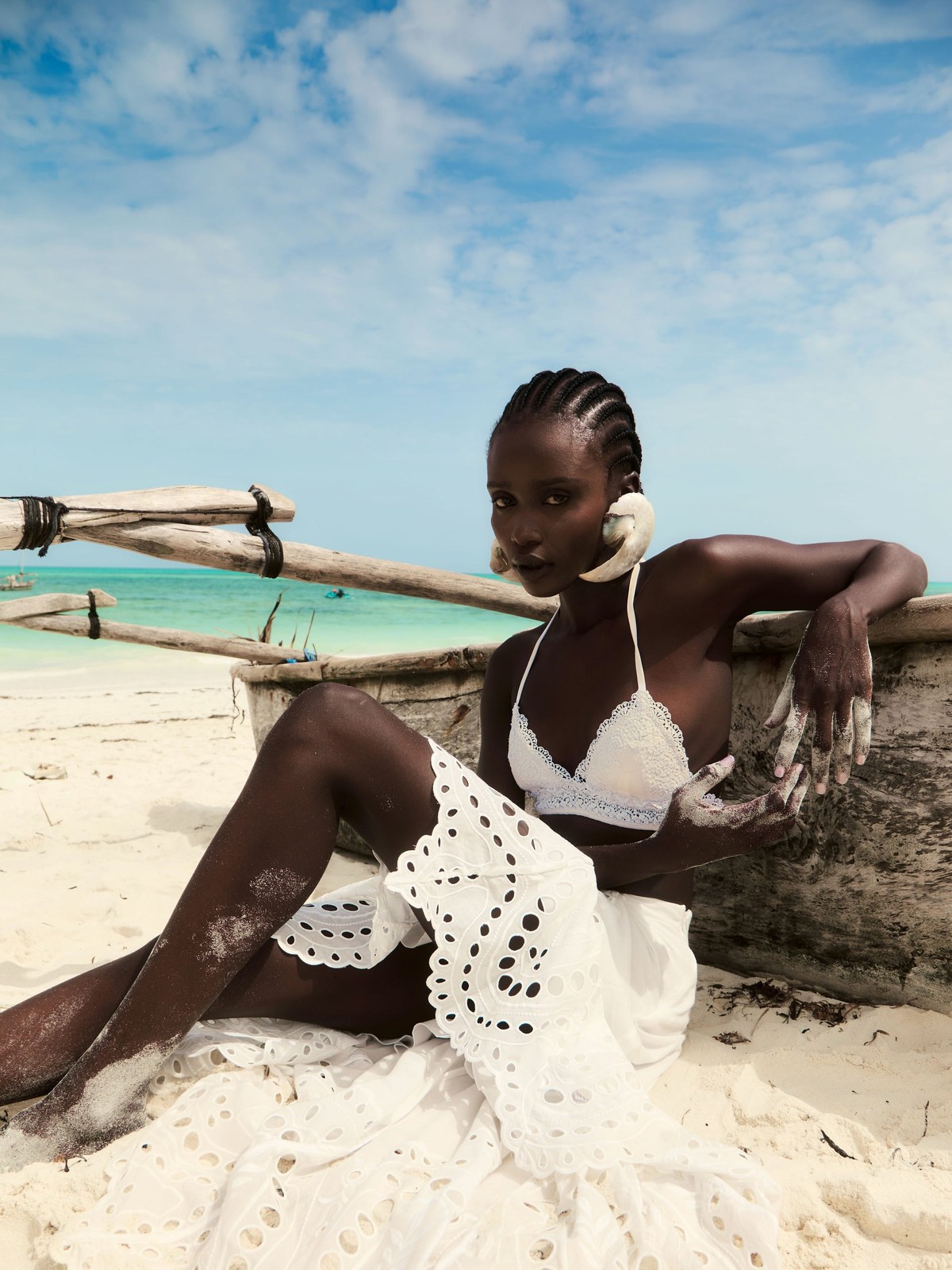 Model in a white cutwork look sitting on a Zanzibar beach