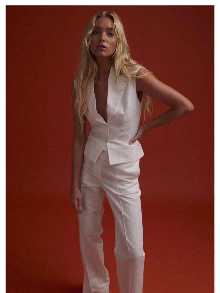 Model in a white Aya Muse suit against a rust-red studio background
