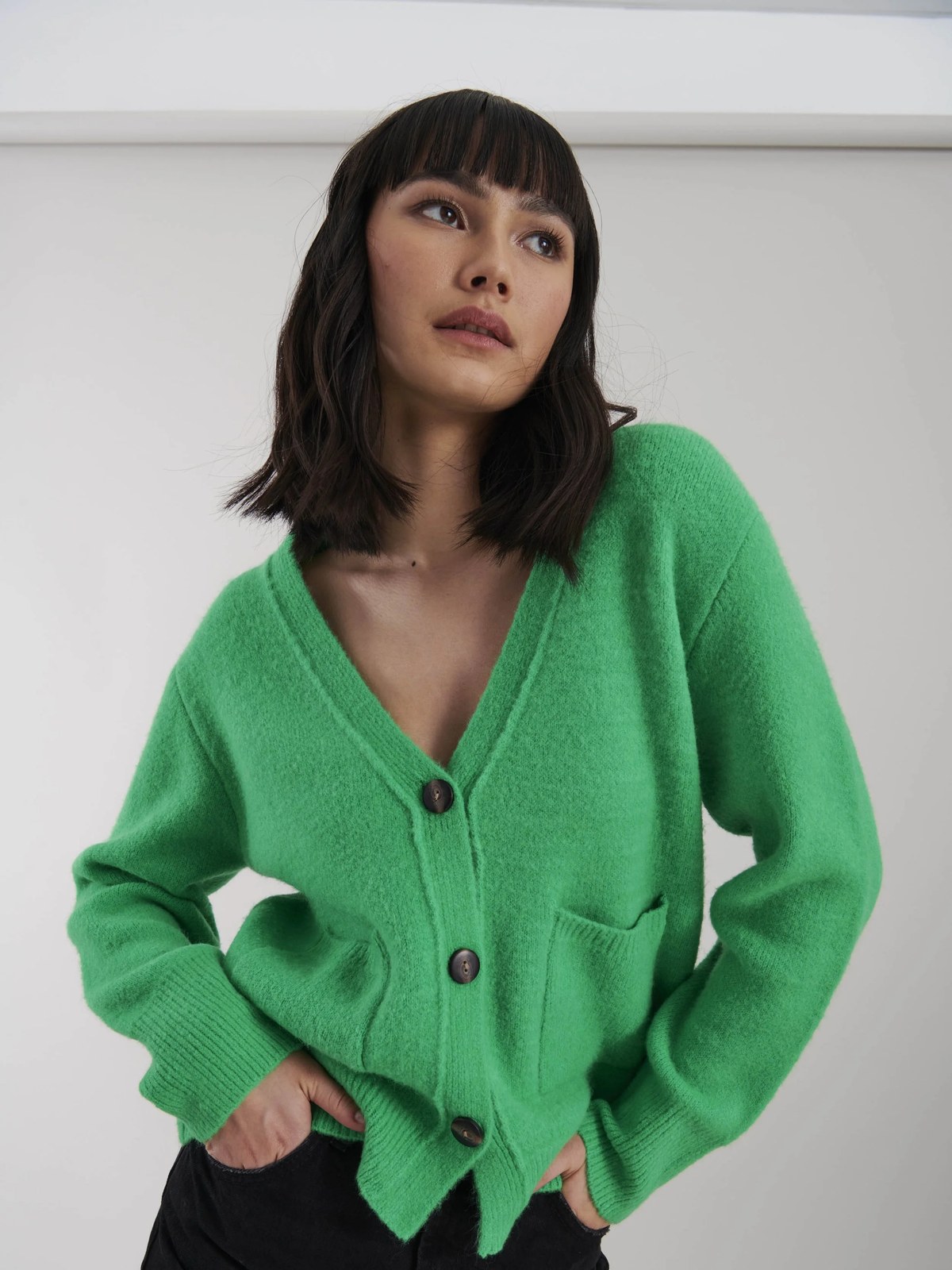 Model wearing a bright green cardigan with dark trousers