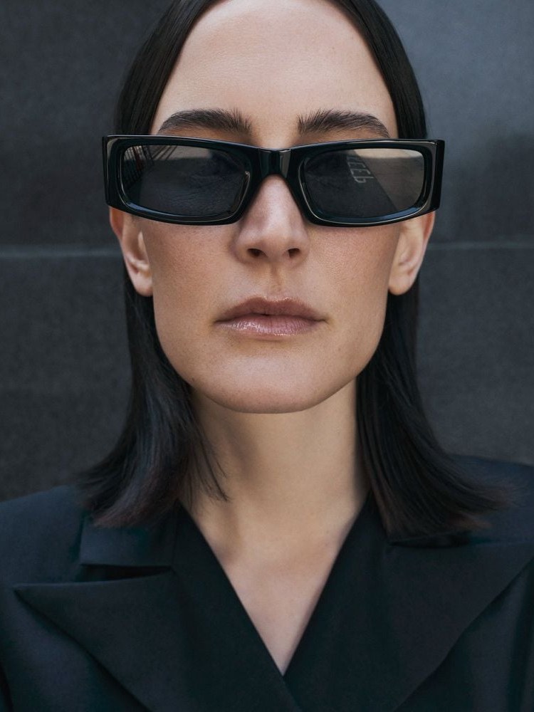 Model in oversized black sunglasses and a sharply tailored black jacket