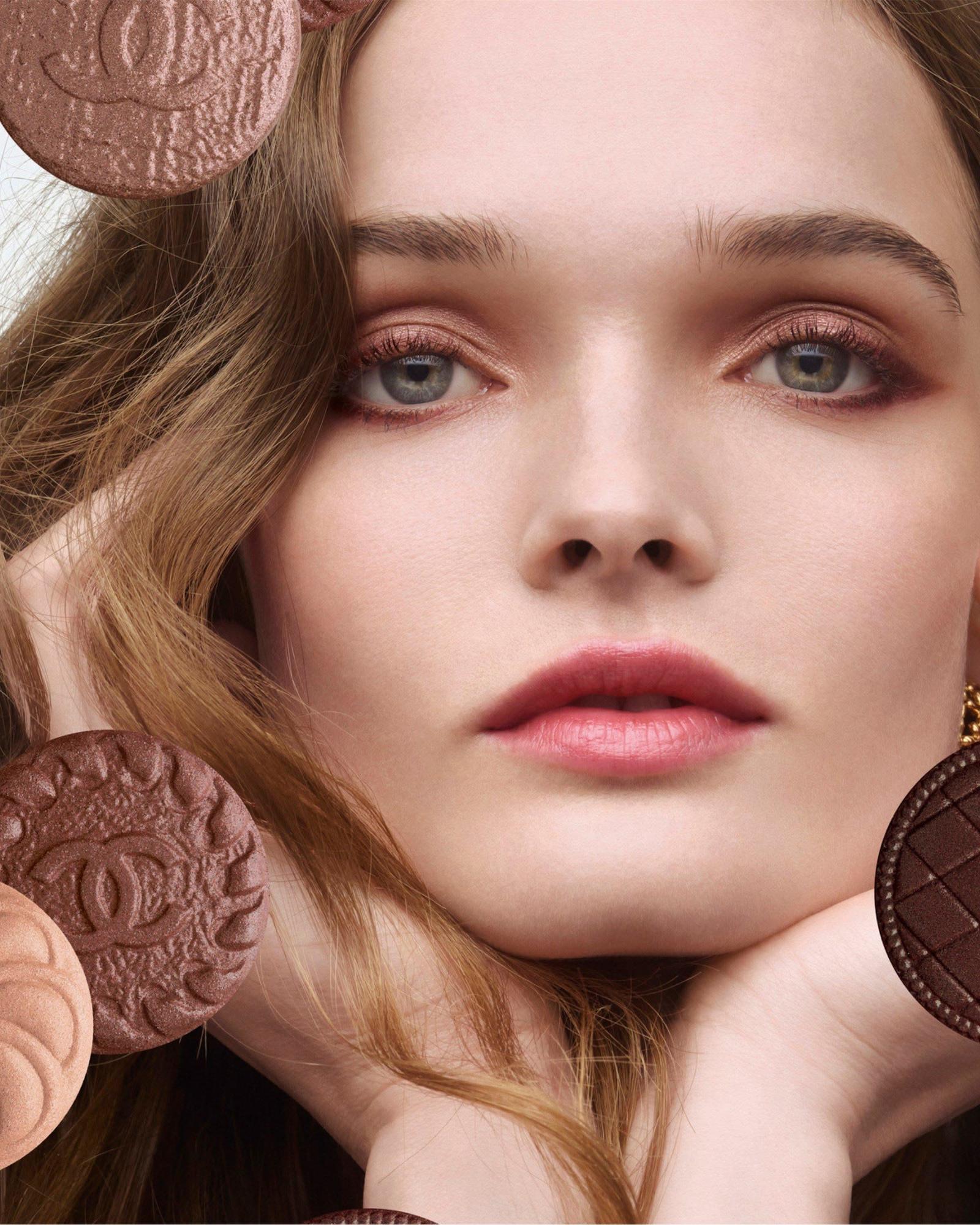 Close up of a woman with bronze eyeshadow and rosy lips surrounded by embossed brown powder compacts