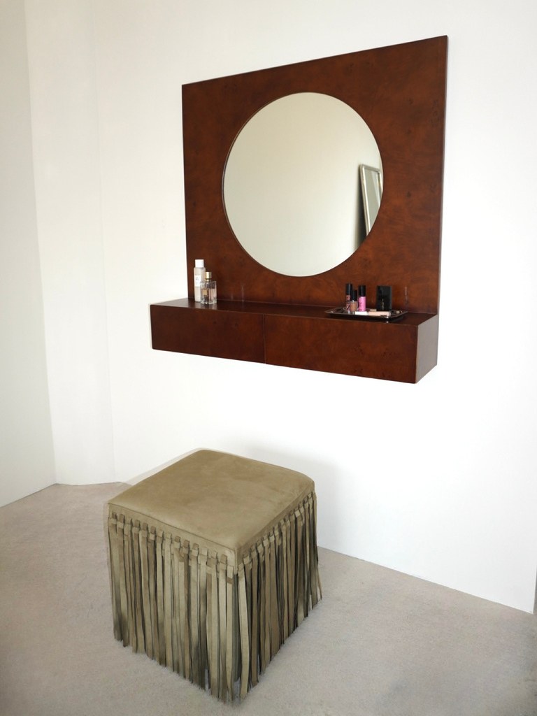 Wood-framed round mirror and fringed ottoman styled in a light room
