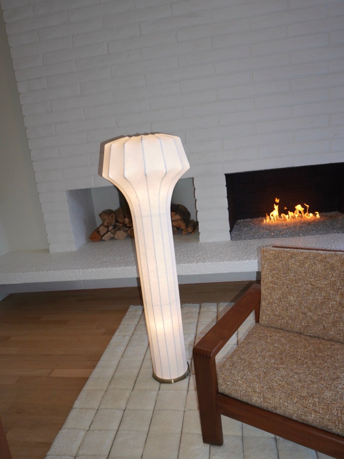 Sculptural floor lamp beside a chair and lit fireplace in a calm living room