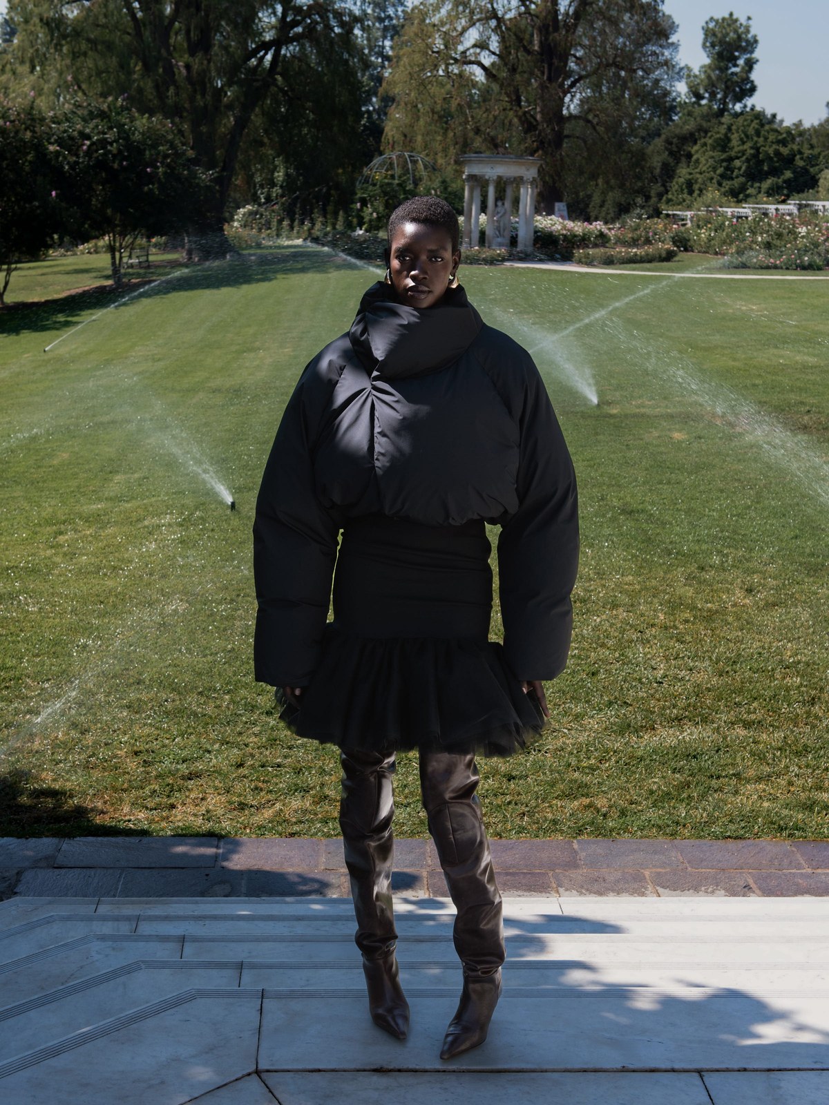 Model in a black puffer and skirt standing in a formal garden
