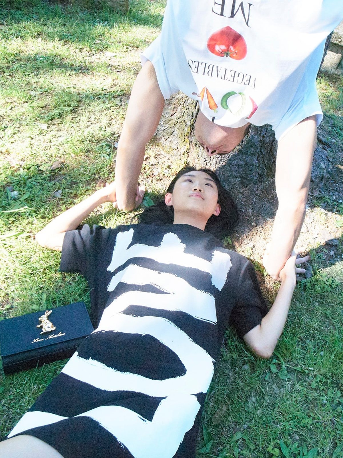 Model lying on grass in a black and white brushstroke print dress beside a second model upside down in a graphic tee