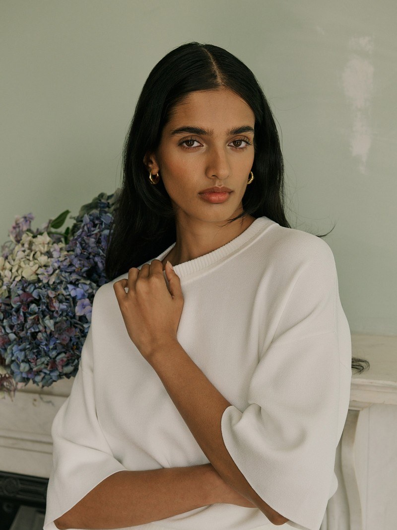 Model in a soft white CLEA top with flowers behind her
