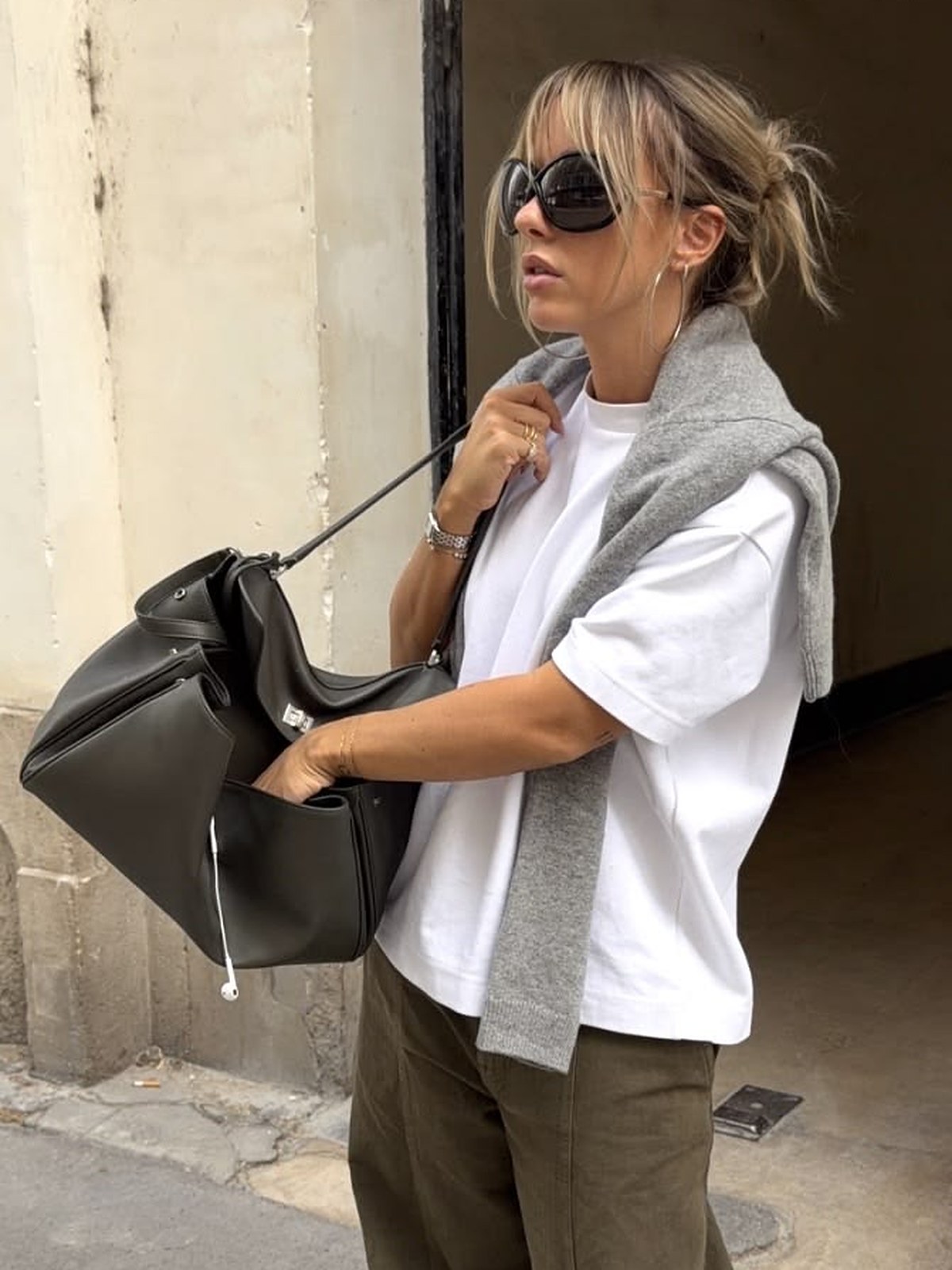 Woman in a white tee with a gray sweater over her shoulders holding a large black bag