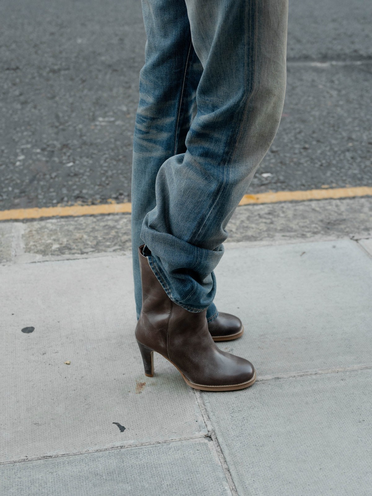 Model wearing dark brown heeled boots with cuffed blue jeans on a city sidewalk