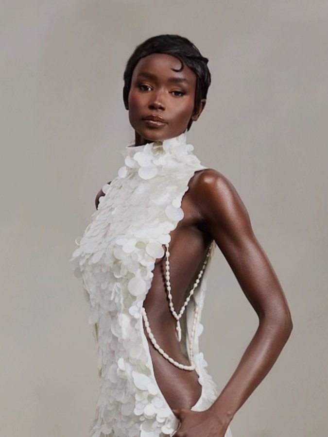 Model with short hair in a white sequin dress with side cutouts against a gray studio background