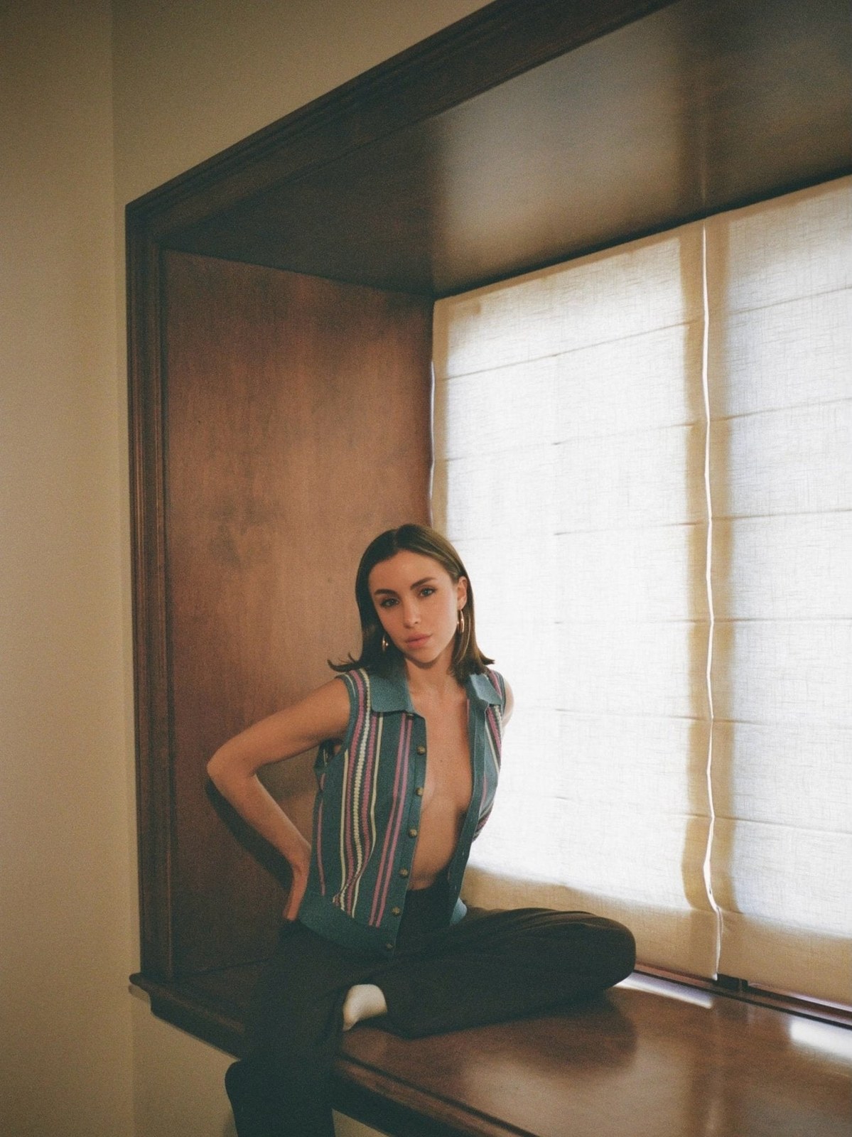 Woman in a striped sleeveless top seated beside a bright window