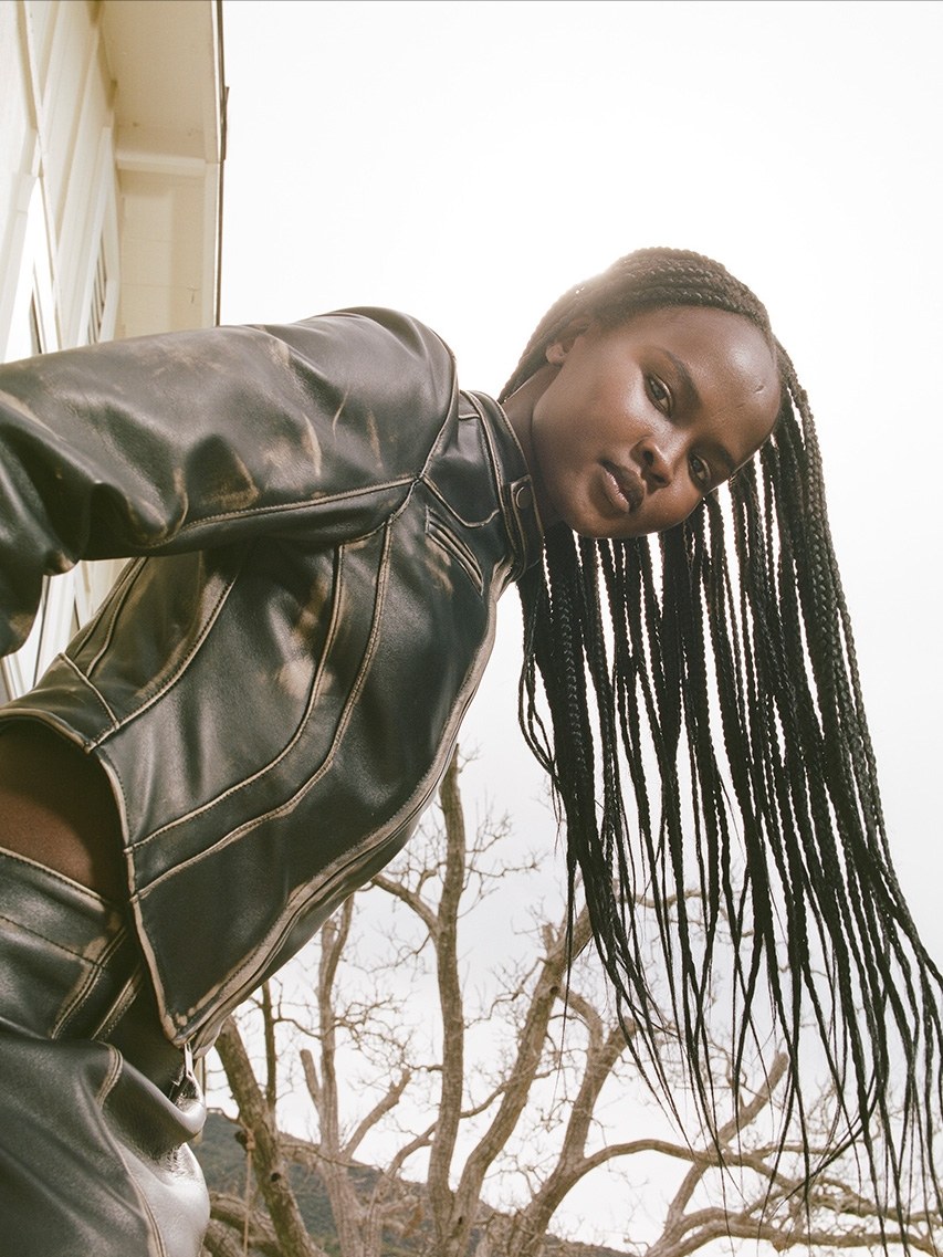Model in a dark leather jacket leaning toward the camera outdoors