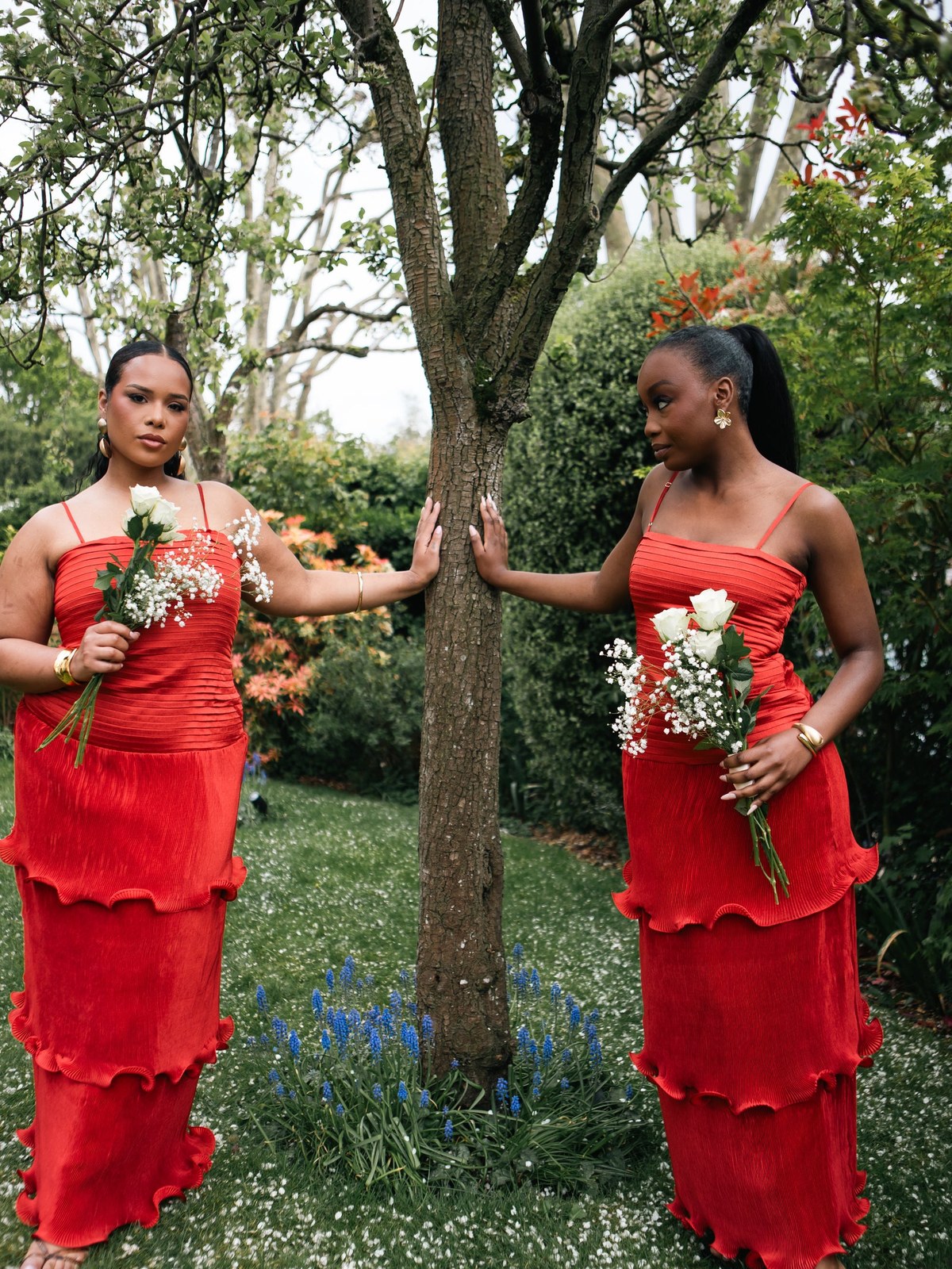 Two women in red dresses outdoors with bouquets