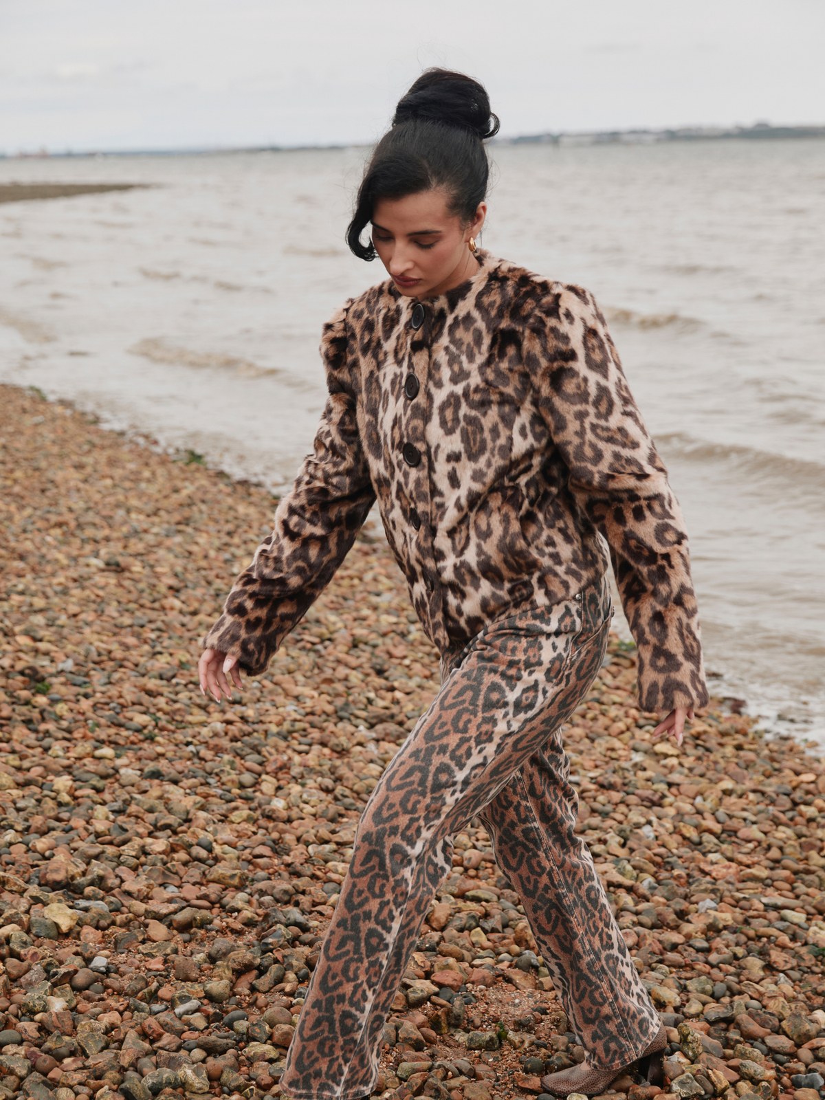 Model in a leopard print House of Sunny set walking on a pebbled beach