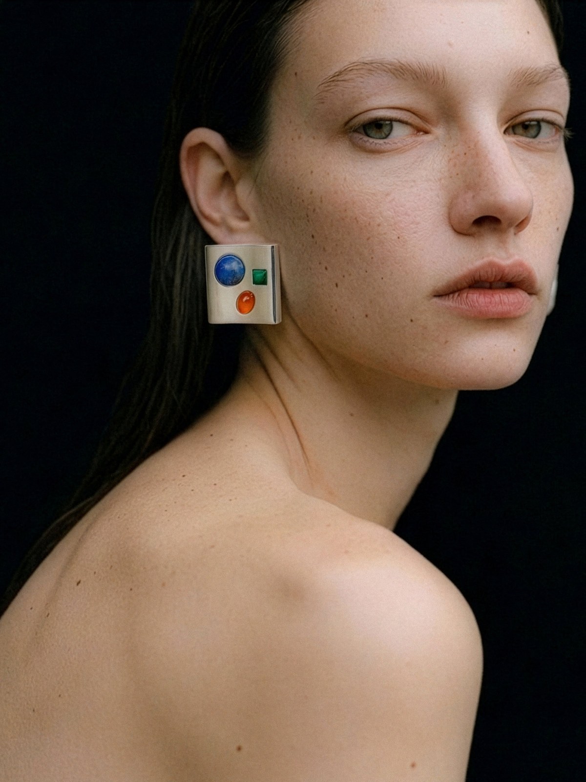 Model wearing a colorful sculptural earring against a dark studio background