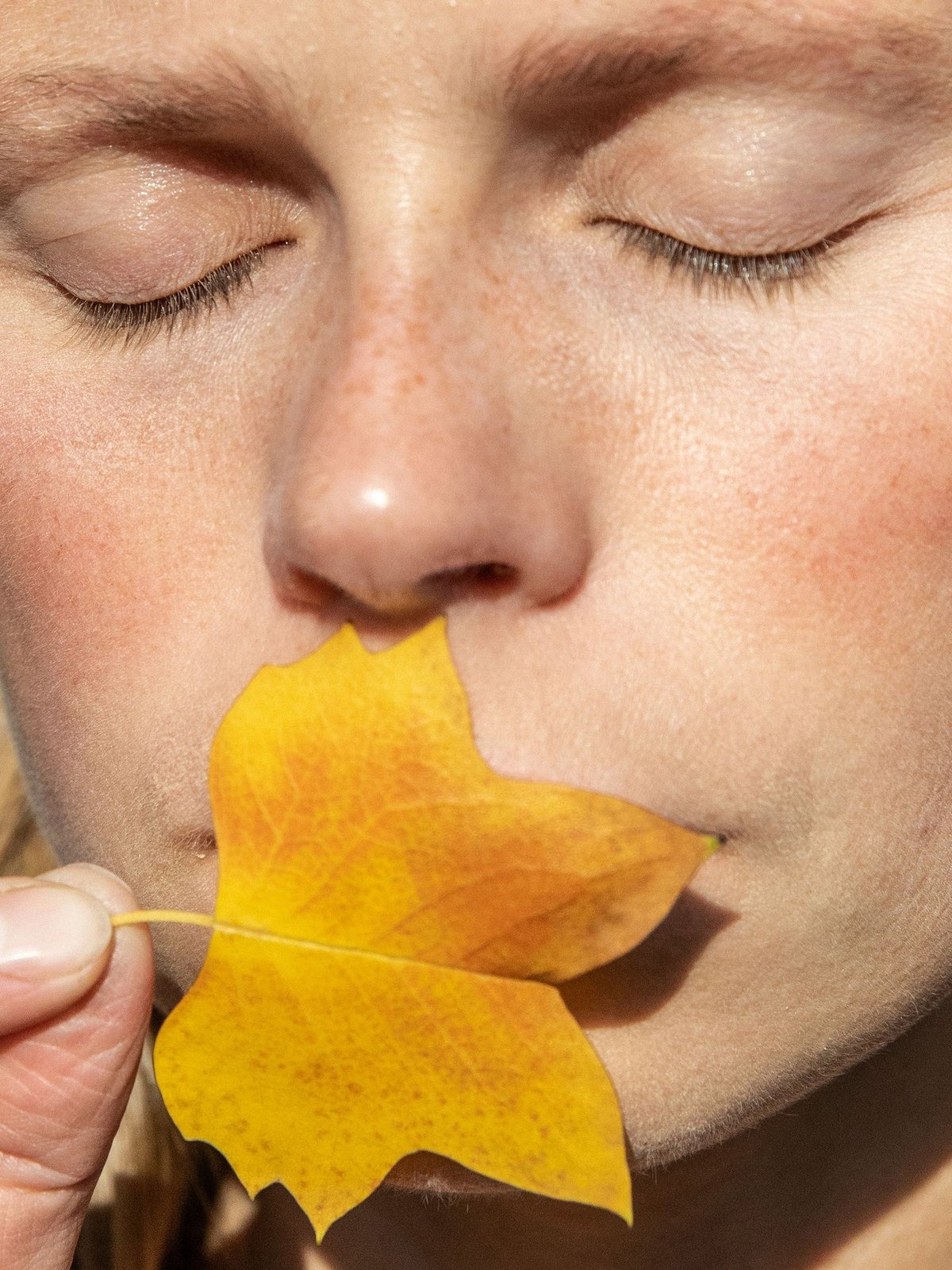 Close-up portrait of a woman with eyes closed and a yellow leaf at her lips