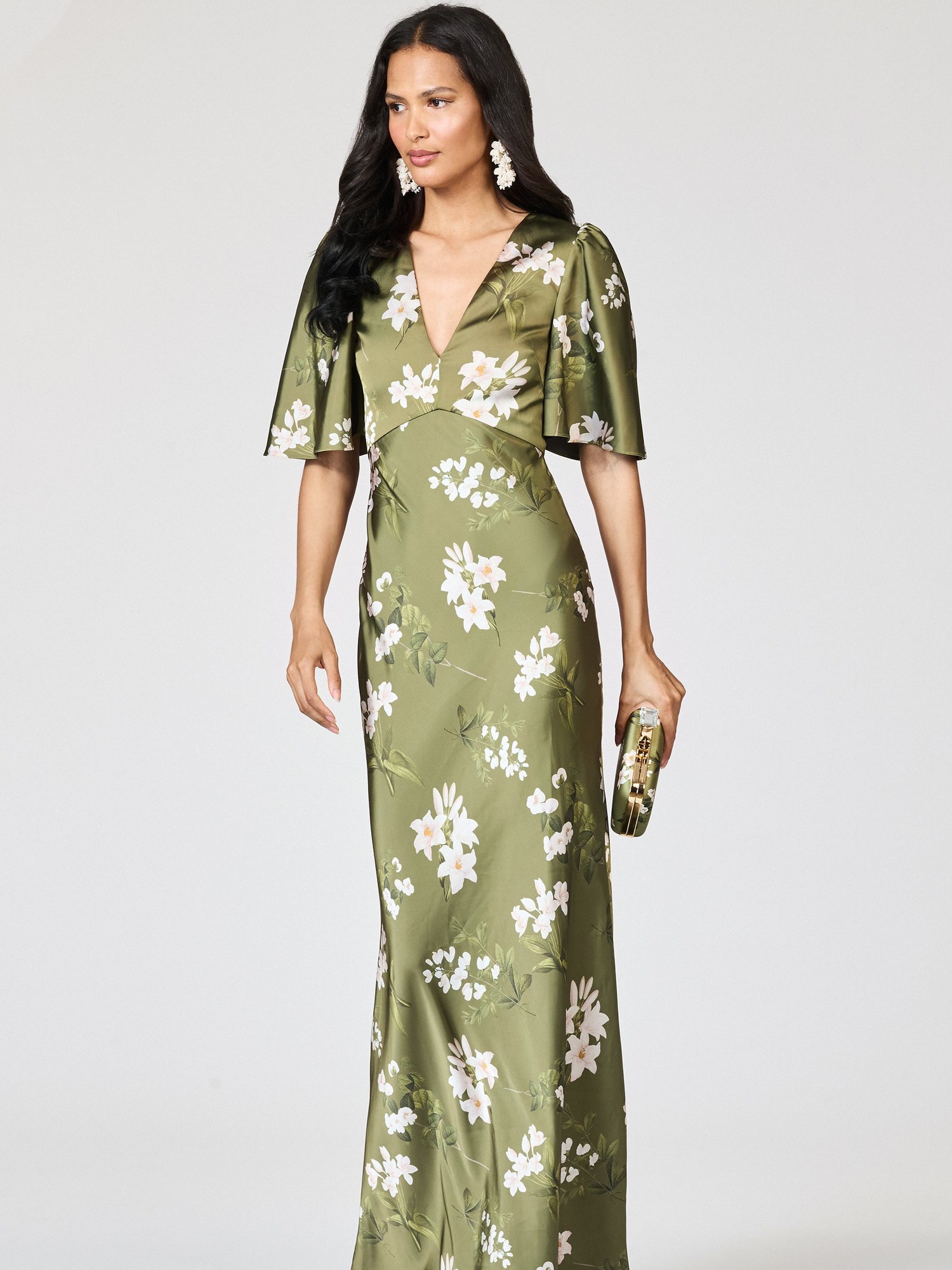 Model in an olive green floral satin gown with flutter sleeves holding a clutch