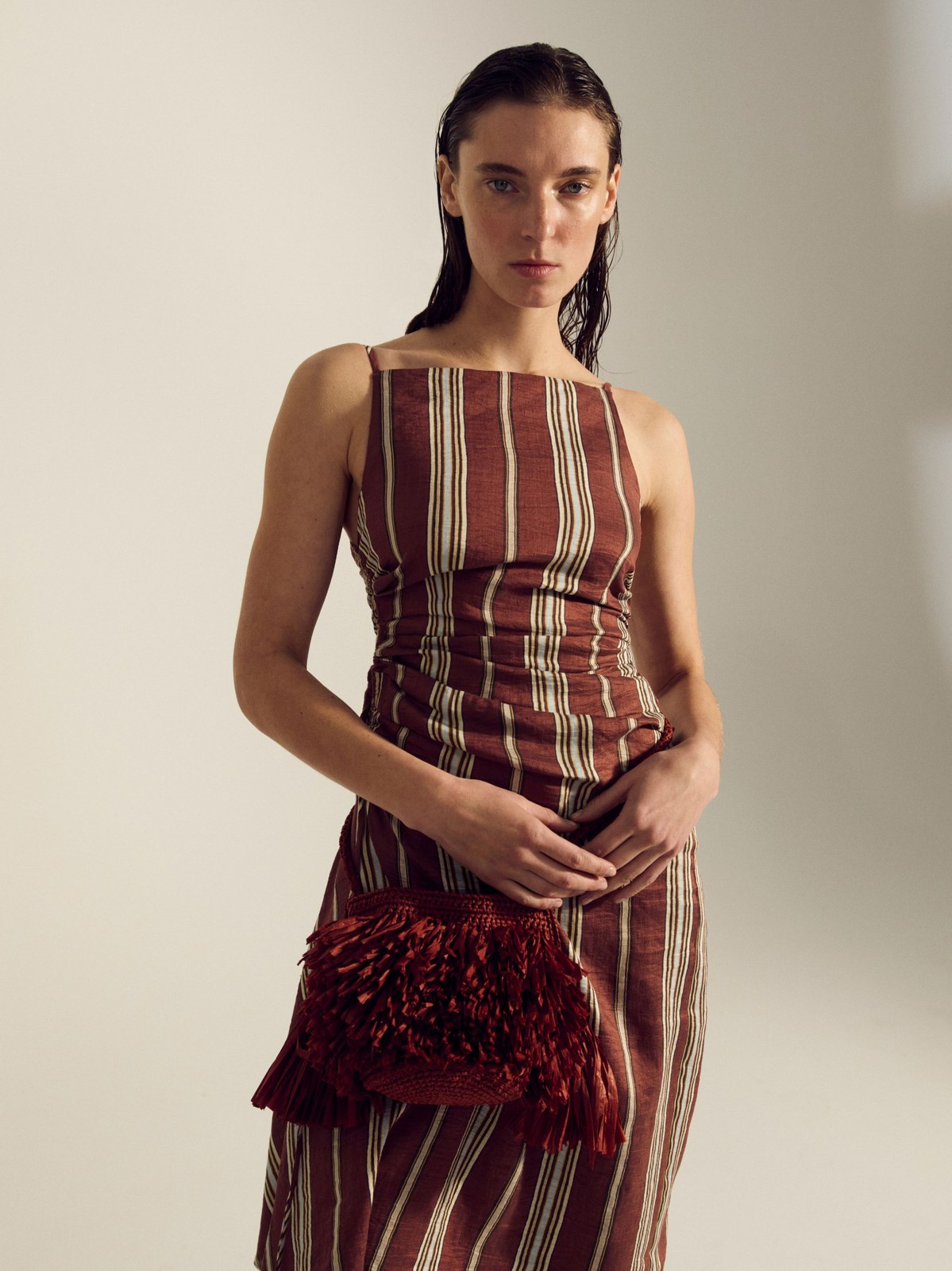 Model in a striped burgundy gown holding a fringed evening bag