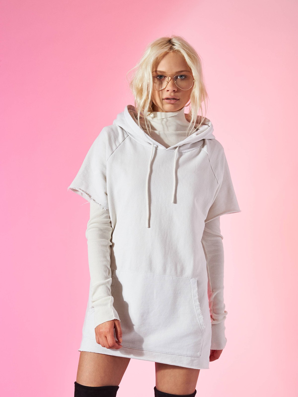 Model in a white hooded tunic against a pink studio backdrop