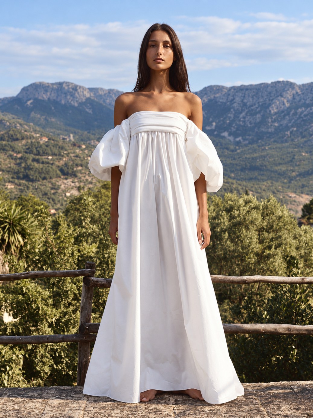 Model in an ivory gathered gown against a mountain terrace.