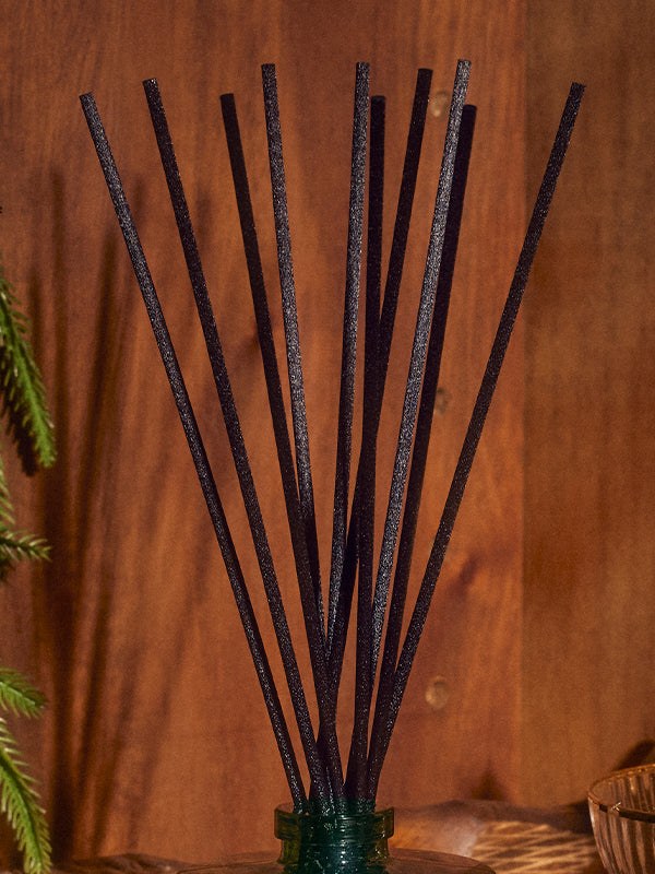 Reed diffuser among evergreen branches and warm wood in a softly lit room