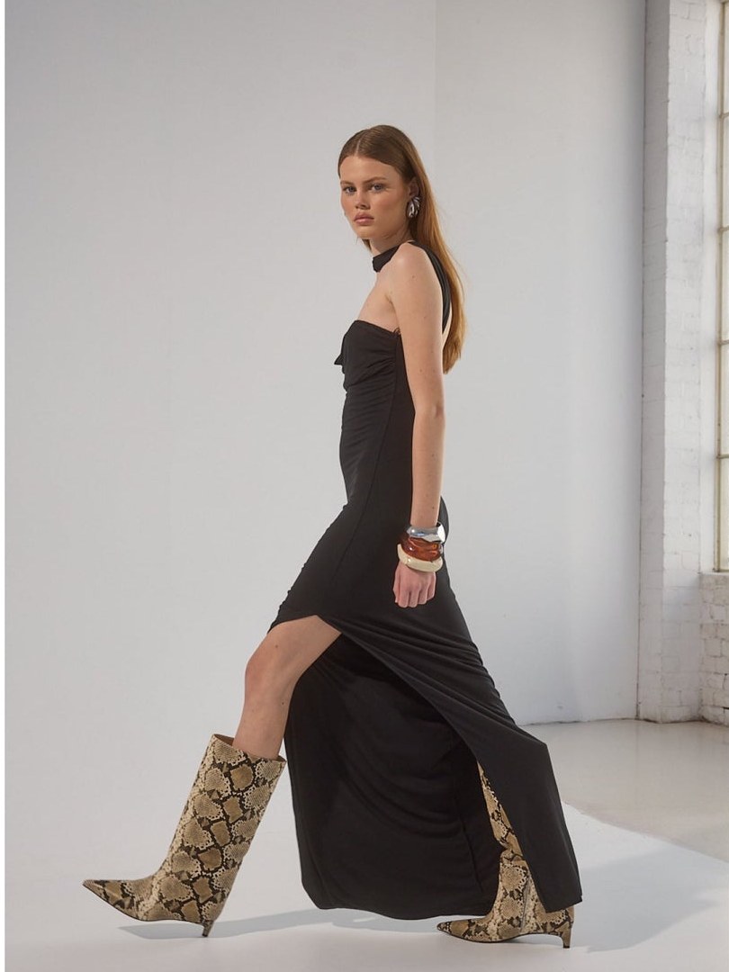 Model walking in a long black dress and patterned boots in a light studio