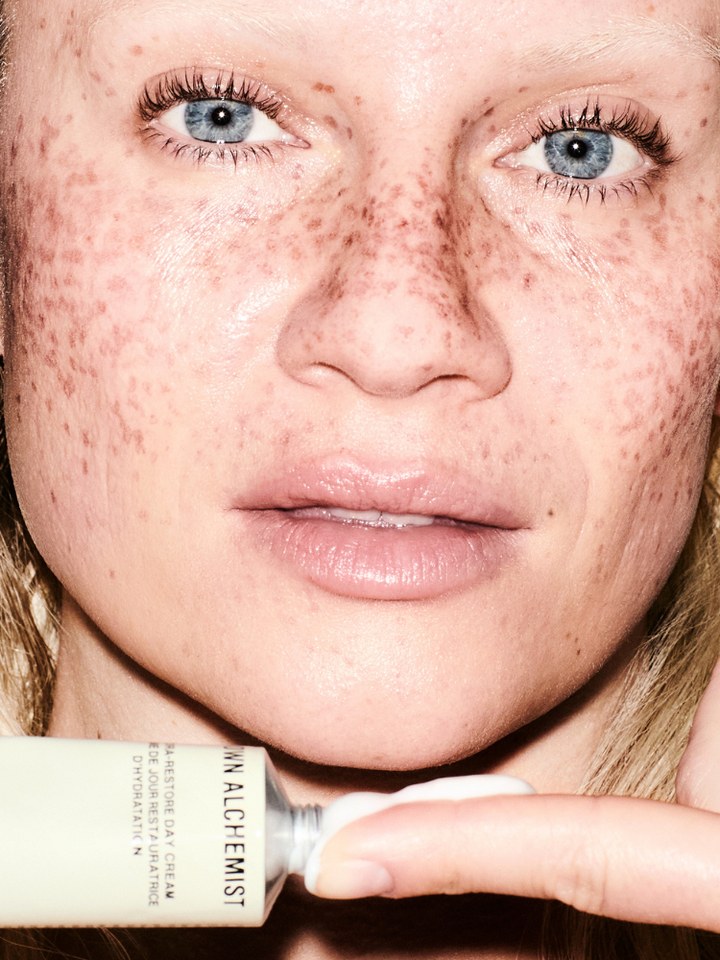 Freckled model holding a Grown Alchemist skincare tube in a close-up beauty portrait