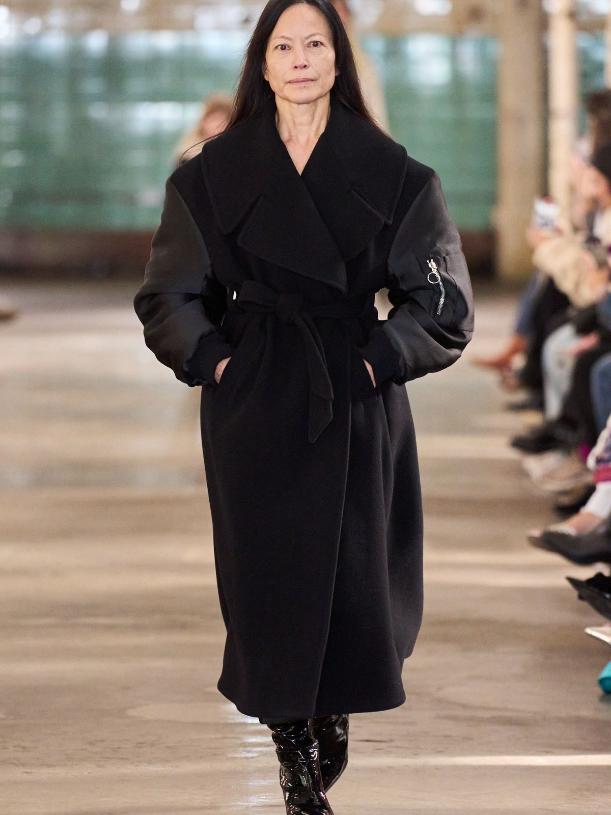 Model in a long black belted coat on the runway