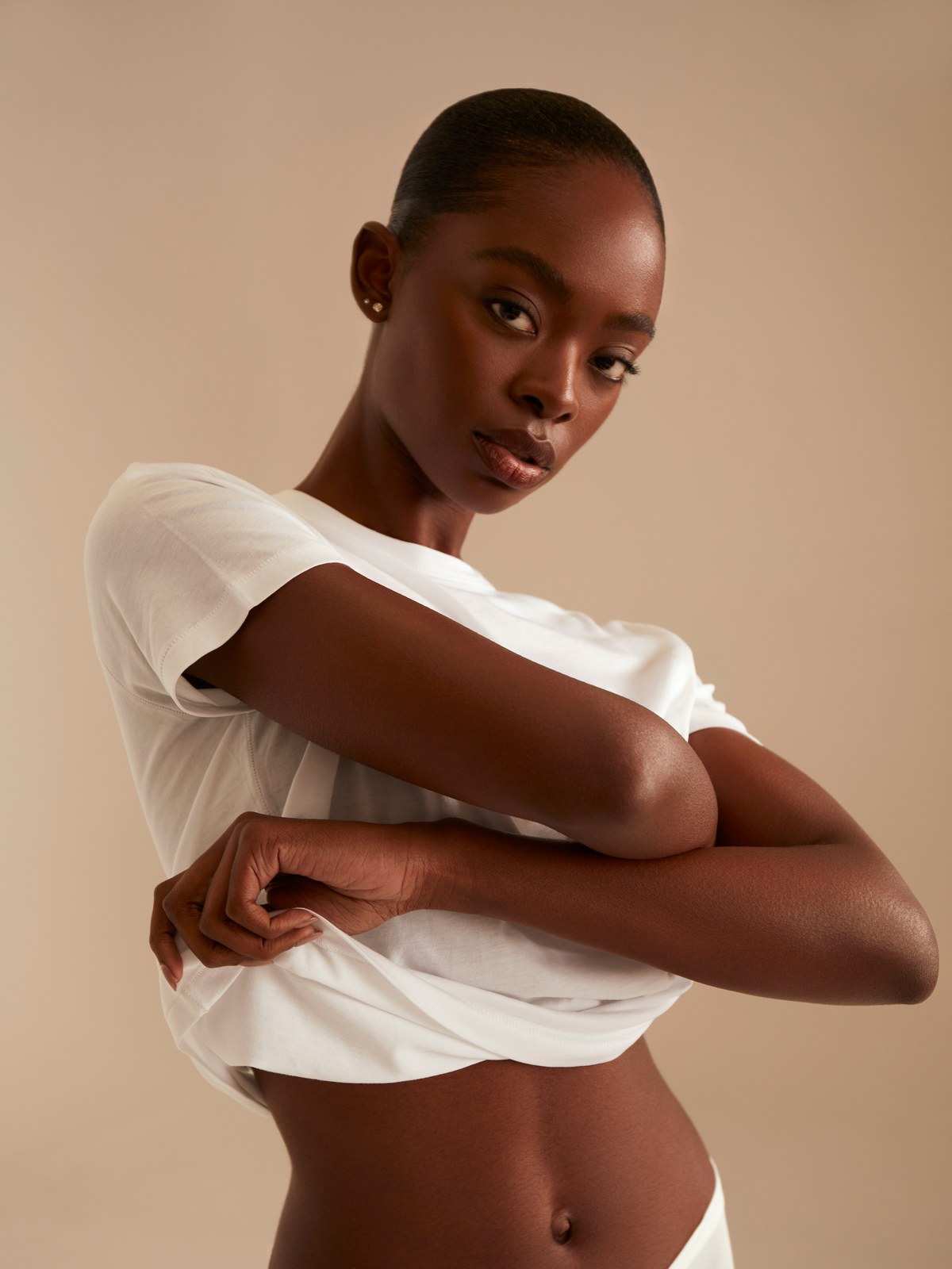 Woman in a white TKEES tee standing against a warm studio backdrop