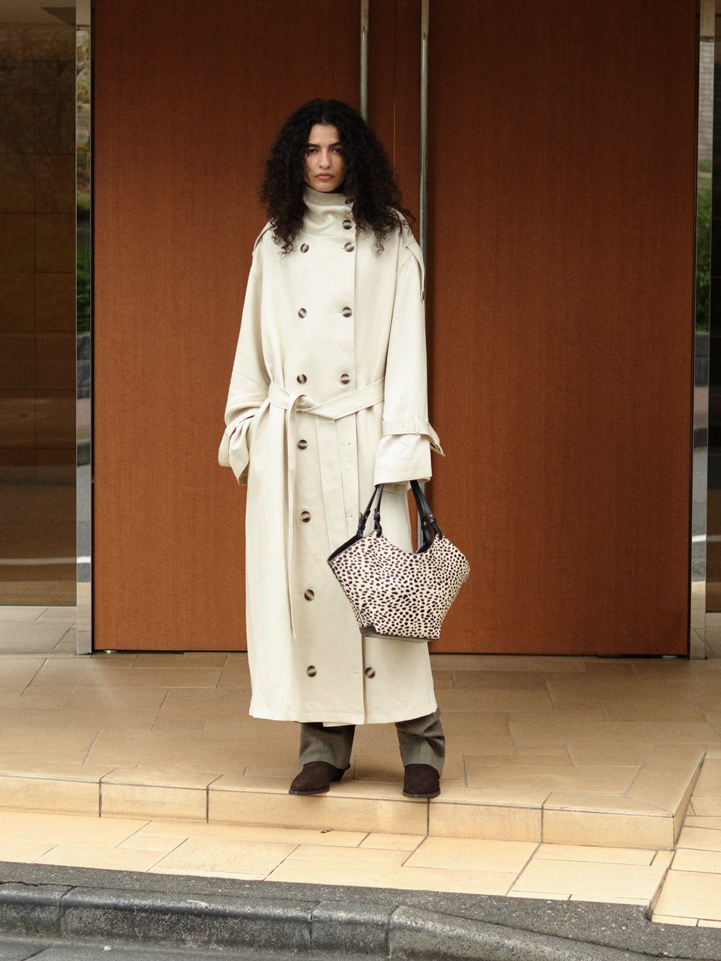 Model in a long white coat carrying a patterned handbag