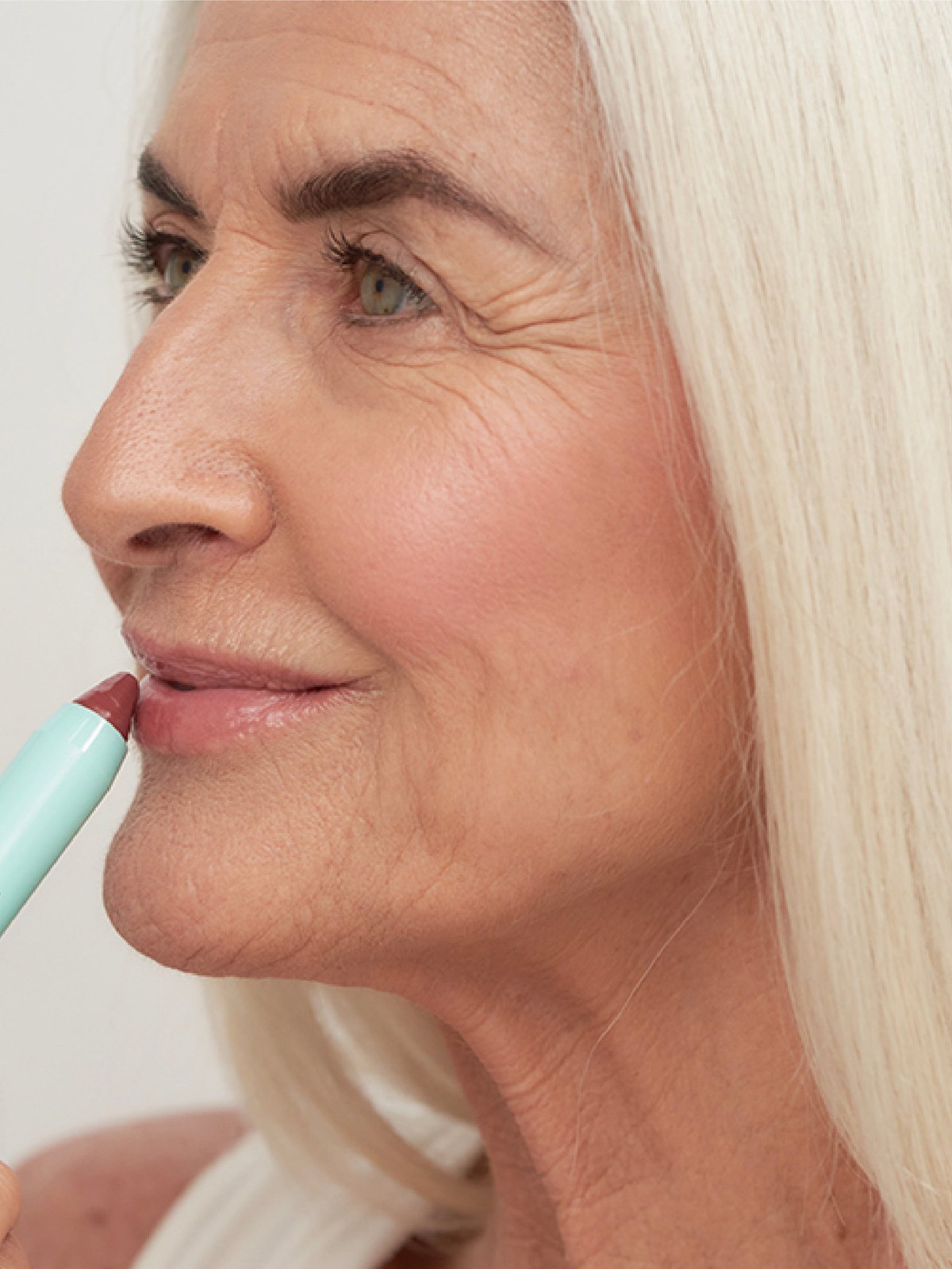 Mature model applying a mint SWEED lip pencil in profile