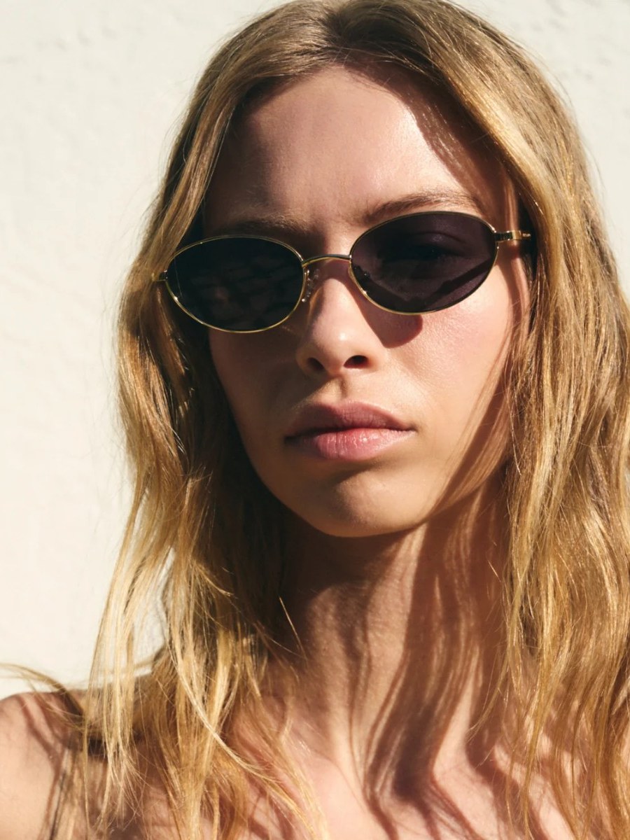 Model wearing rounded sunglasses in a sunlit studio portrait