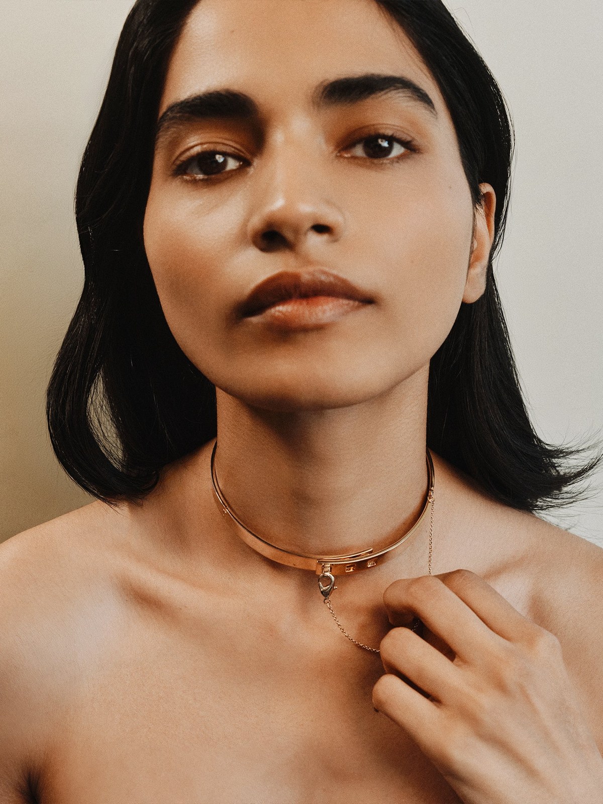 Model wearing a pendant necklace and holding its chain at her collar
